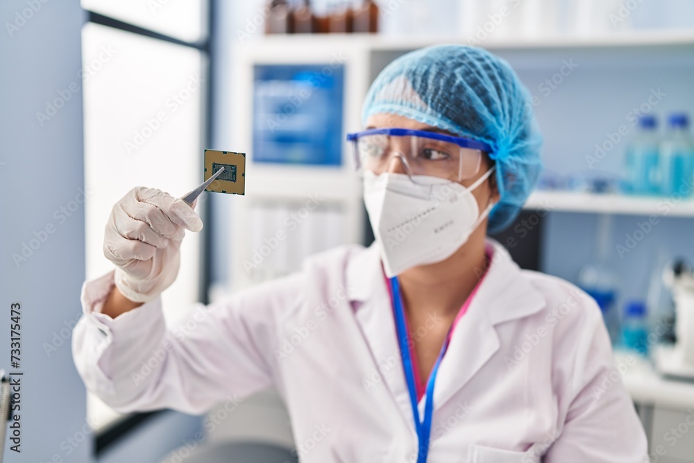 Young beautiful hispanic woman scientist wearing medical mask holding cpu processor chip at pharmacy Young beautiful hispanic woman scientist wearing medical mask holding cpu processor chip at pharmacy
