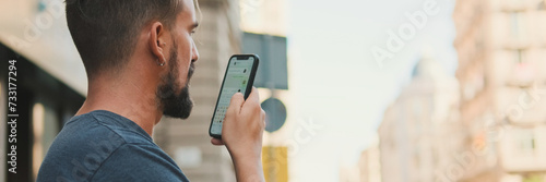 Close-up young man with beard uses cellphone while standing on crosswalk, sends voice message, Panorama