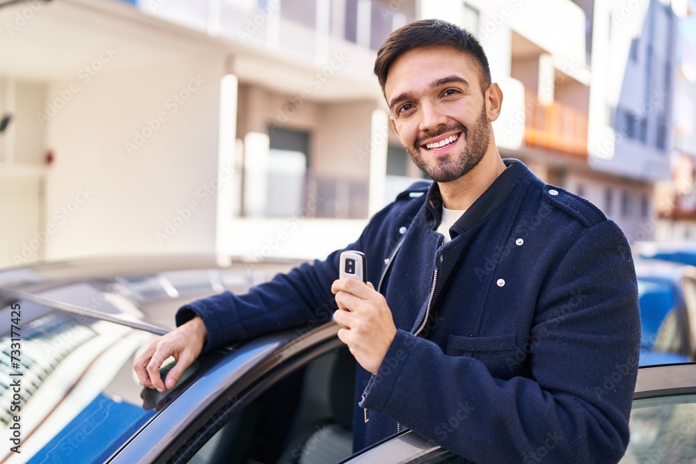 Young hispanic man smiling confident holding key of new car at street