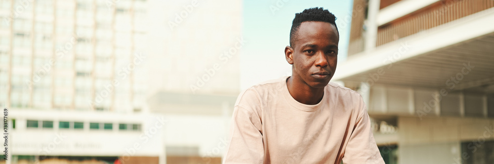 Smiling young african student sitting outside of university, looking at camera, Panorama Smiling young african student sitting outside of university, looking at camera, Panorama