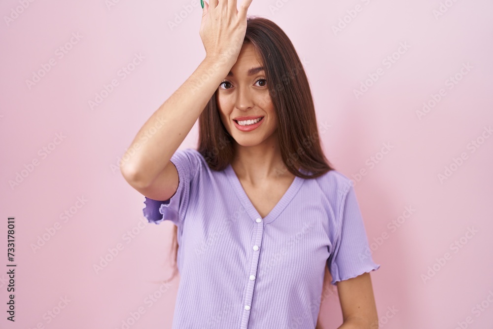 Young hispanic woman with long hair standing over pink background surprised with hand on head for mistake, remember error. forgot, bad memory concept. Young hispanic woman with long hair standing over pink background surprised with hand on head for mistake, remember error. forgot, bad memory concept.