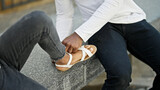 African american father and daughter sitting on bench putting shoe at street