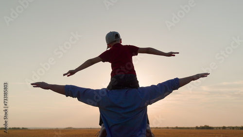 Father Son play together in front of sun, dream, fly. Dad, child fantasize, kid aviator sits on his fathers shoulders. Concept of happy family, childhood dream. Boy plays pilot airplane, hands wings
