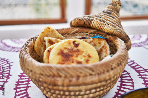 A traditional moroccan wicker bread basket filled with fresh khobz on an embroidered tablecloth. photo