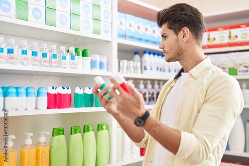 Young hispanic man customer holding toothpaste bottles at pharmacy