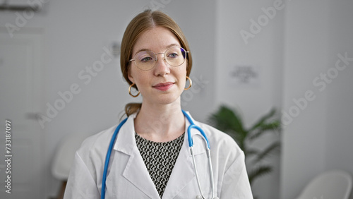Young blonde woman doctor standing with serious expression at clinic waiting room