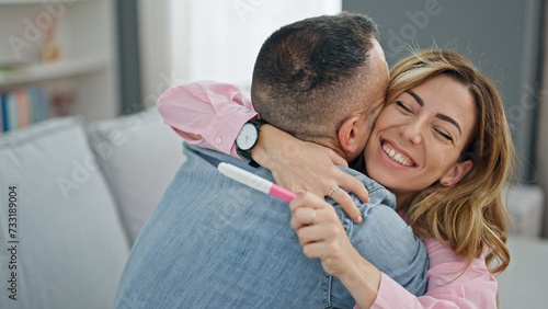 Man and woman couple holding pregnancy test celebrating at home photo