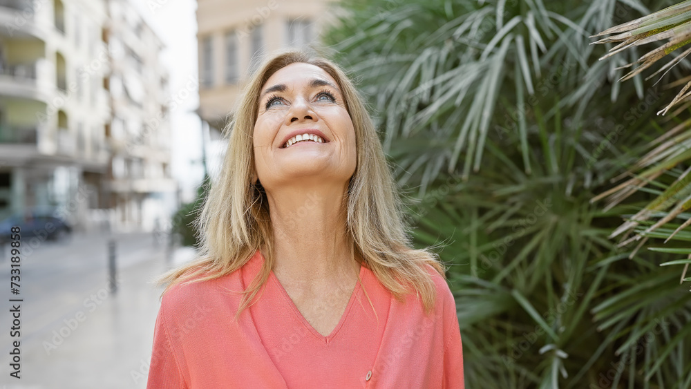 Smiling mature woman in casual wear enjoying a sunny day in an urban environment.
