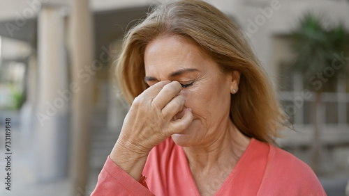 Mature caucasian woman looking stressed touching her nose on a sunny city street.