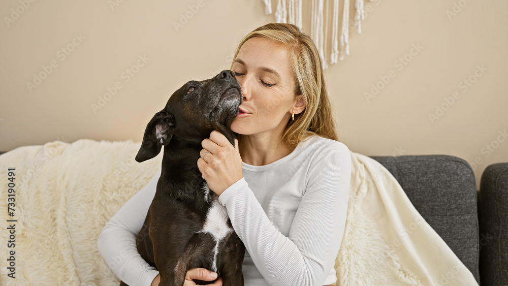 A blonde woman affectionately kissing her black dog on a sofa, depicting love and companionship in a cozy home setting. A blonde woman affectionately kissing her black dog on a sofa, depicting love and companionship in a cozy home setting.