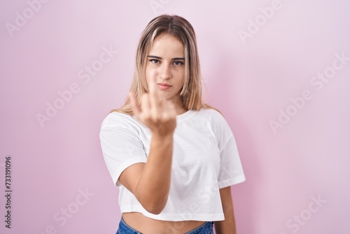 Young blonde woman standing over pink background showing middle finger  impolite and rude fuck off expression