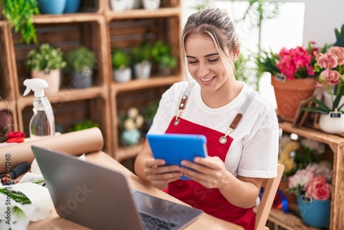 Young blonde woman florist smiling confident using laptop and touchpad at flower shop