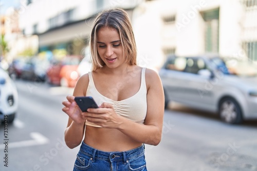 Young blonde woman smiling confident using smartphone at street