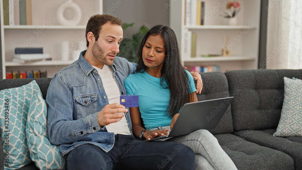 Beautiful couple shopping with laptop and credit card sitting on sofa at home