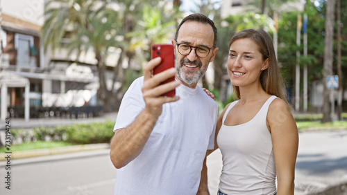 Confident father and daughter share a lovely moment, joyfully taking a cool selfie on their mobile phone standing on a bustling city street.