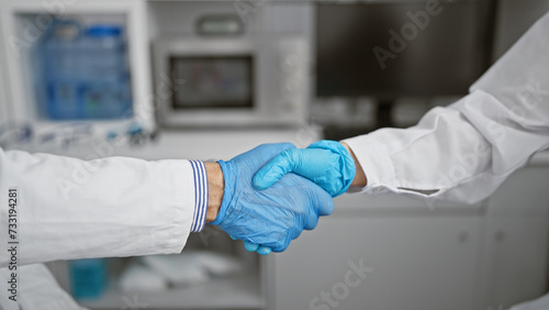 Two enthusiastic scientists shaking hands in agreement, celebrating a groundbreaking medical achievement in their indoor research laboratory.