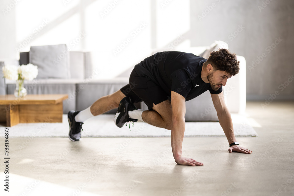 Young man stretching his leg in front of laptop during domestic training, following online video tutorial on laptop Young man stretching his leg in front of laptop during domestic training, following online video tutorial on laptop