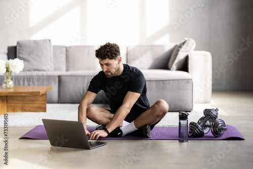 Male fitness instructor showing exercises while streaming, broadcasting video lesson on training at home using laptop.