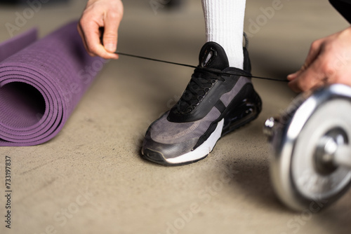 Close up of man in fitness clothing fastening trainers before exercising with hand weights at home