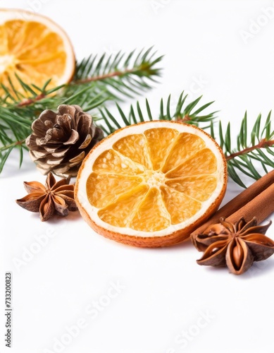 Slices of orange adorned with cinnamon, star anise, and a Christmas tree branch form a festive arrangement on a white background, creating a visually appealing and aromatic holiday scene.