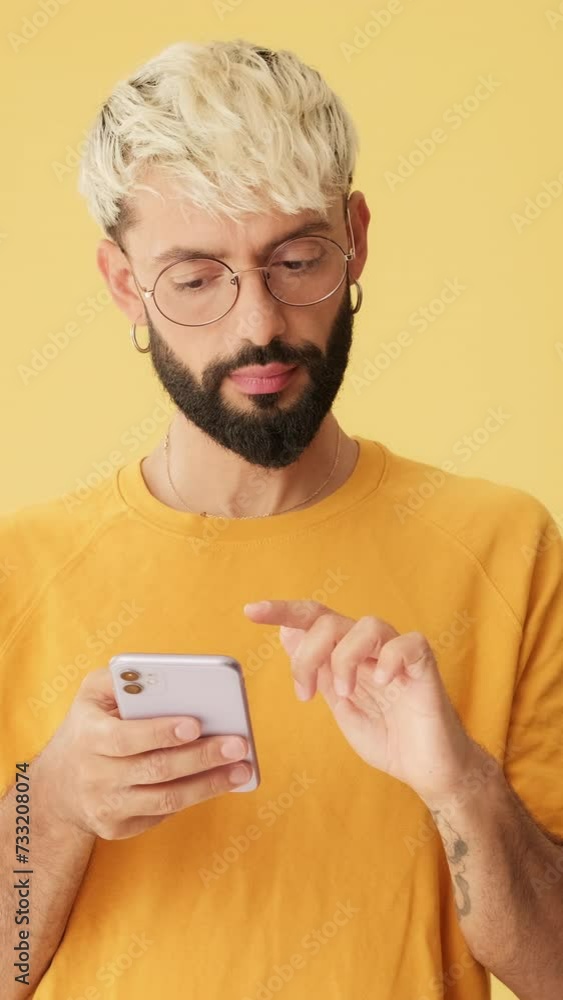 Man with phone in his hands scrolls, chooses, makes purchases isolated on yellow background Man with phone in his hands scrolls, chooses, makes purchases isolated on yellow background