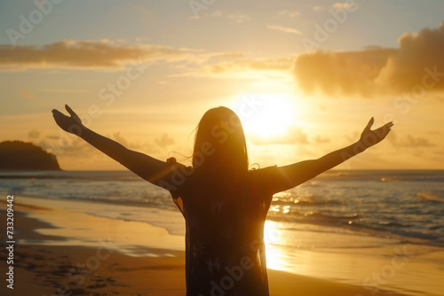 Woman with open arms under the sunrise at seaside wellness concept.