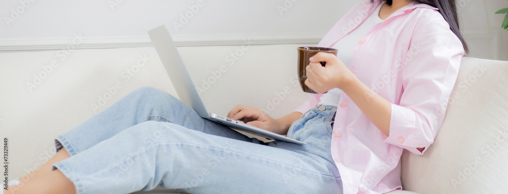 Young asian business woman work from home with laptop computer and drinking coffee on sofa in living room, freelance girl using notebook sitting on couch with comfort and relax, lifestyles concept. Young asian business woman work from home with laptop computer and drinking coffee on sofa in living room, freelance girl using notebook sitting on couch with comfort and relax, lifestyles concept.