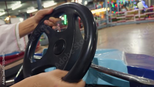 closeup man hand on a bumper car steering wheel with colorful cars in the background at an amusement park photo