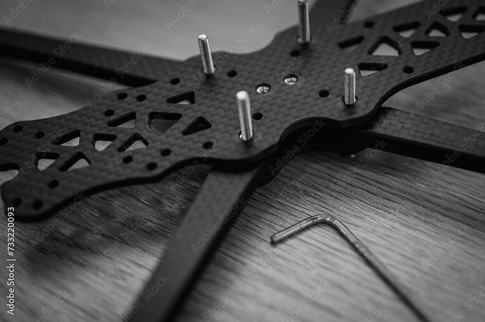 Fototapeta premium Black and white photo, background, top view, twisting drone frame parts, soldering, assembly, fpv drone part assembled by man on wooden background. Close-up, high technology, drones