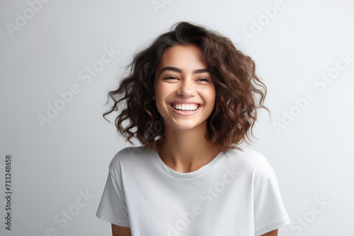 A woman with curly hair happily smiles at the camera, showing her joy and warmth.