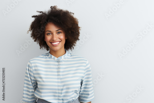 A woman with an afro hairstyle stands confidently in front of a plain white wall.