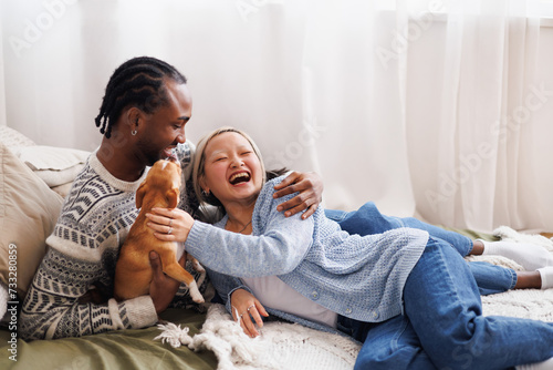 Smiling young interracial couple chilling with dog on bed at home photo