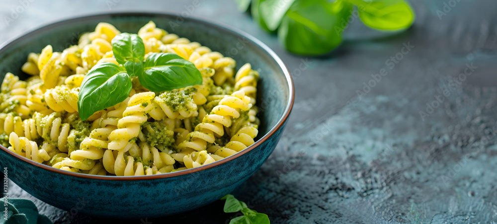 Spiral pasta mixed with vibrant green pesto sauce, garnished with fresh basil leaves in a rustic ceramic bowl Spiral pasta mixed with vibrant green pesto sauce, garnished with fresh basil leaves in a rustic ceramic bowl