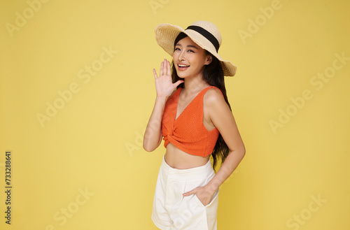 Portrait smiling attractive Asian woman in summer dress and hat posing open mouths raising hands screaming announcement isolated on yellow background.