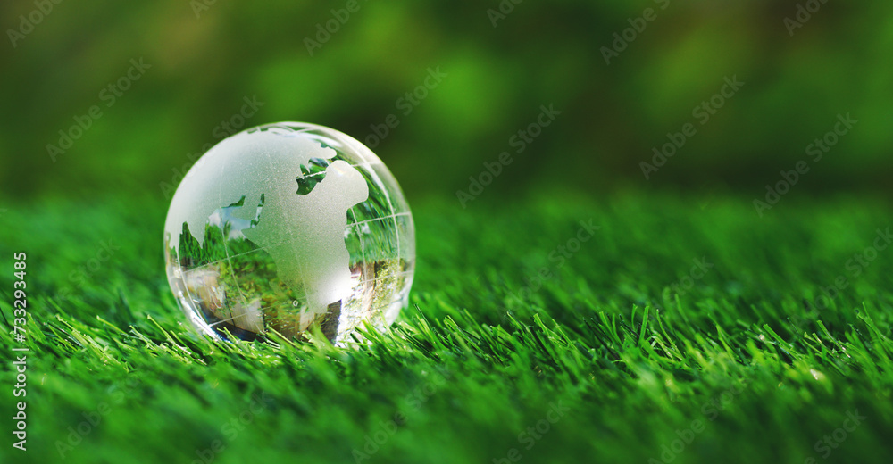 Glass earth globe crystal on green grass in the garden of safe world, save the planet concept, ecological, recycle, nature, environment friendly and World Environment Day. Close up with copy space.