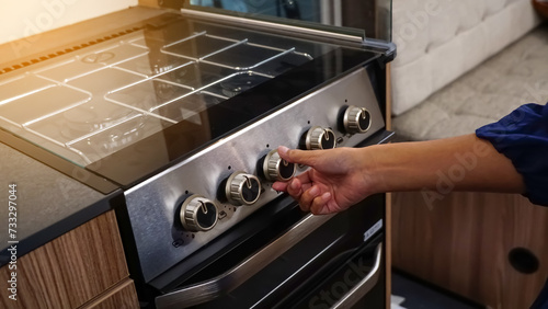 Woman hand turning switch knob on gas stove for opening or closing modern electric oven prepare to cooking in the modern kitchen.