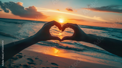 Couple hands making heart symbol on sunset beach background, love and compassion concept. photo