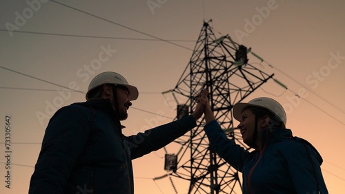 Builders Energy in protective helmets inspect iron structure of power line. Teamwork, business project for construction of electrical communications. Engineers shake hands. Power engineer woman man