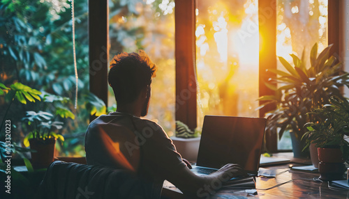 Man working on his laptop sitting at a desk overlooking a tropical setting. Digital nomad working in tropical countries, working from abroad, working remotely. Expat working at a vacation spot. 