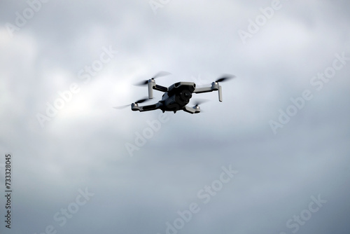 Fototapeta Naklejka Na Ścianę i Meble -  Four engine drone with camera is flying in the grey stormy cloudy sky front view close up