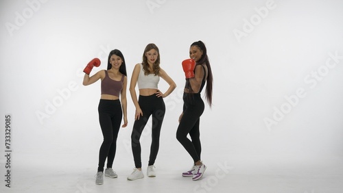Portrait of young multiethnic models isolated on white studio background. Group of three positive multiracial girls posing in boxing gloves at camera. Multiethnic beauty concept.