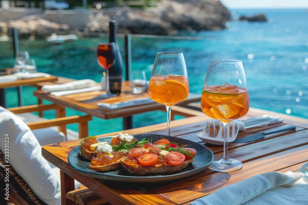An idyllic vacation scene captured in one frame - a wooden table adorned with tableware, a delicious meal and two glasses of wine, set against the backdrop of the sea, creating a perfect outdoor cock