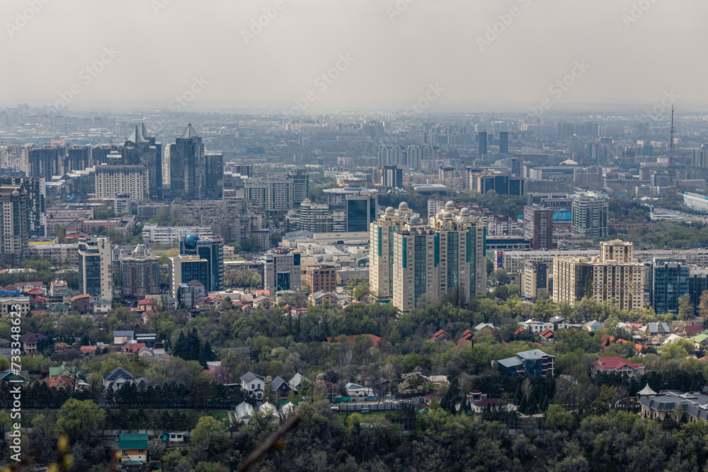 Panoramic view on Almaty from mount Kok Tobe park. Cityscape at spring day. Haze smog above town, ecology problem. Republic of Kazakhstan, Central Asia. City architecture, urban space.