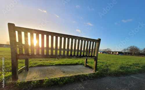 early spring morning in the park, the sun's rays illuminate the grass and bench © yelantsevv