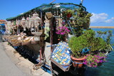 Una barca en un muelle llena de artículos de turistas a la venta, con plantas, imanes y esponjas para vender