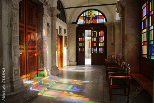 Entrada a una iglesia con una puerta de fondo y ventanas con vidrieras, donde entra la luz dejando el reflejo de los colores photo