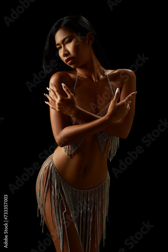 Naked asian girl in transparent dress with rhinestones on threads isolated on the black background
