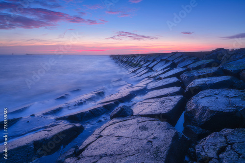 A seascape during sunset. The stone causeway during sunset. Sharp rocks. Bright sky during sunset. Long exposure. Photo for wallpaper.