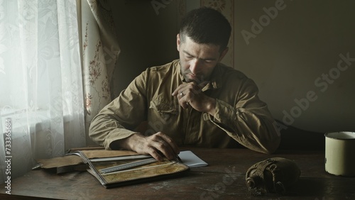 A Soviet Army soldier sits at a table in an abandoned farmhouse and looks at a map of the area. Reconstruction of the events of World War II intelligence soldier. © procinemastock