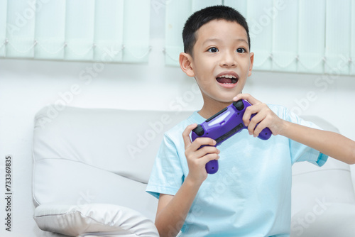 little Asian boy playing a video game. shot of a child holding a game controller. A kid is smiling and playing happily.